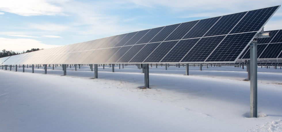 A row of solar panels mounted on top of a field covered by snow.