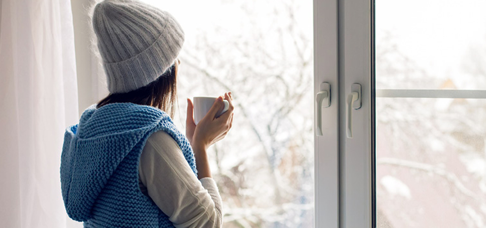 A woman looking outside her window during the winter.