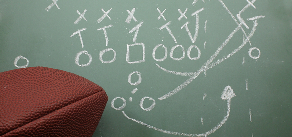 A football next to a diagram of a football play on a chalkboard.,