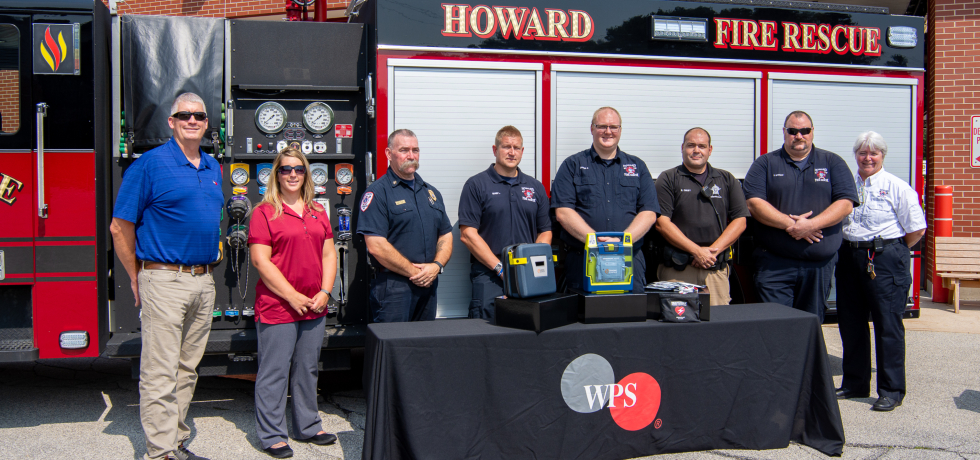 WPS Foundation and Howard Fire Department representatives standing in front of a table with an AED on it.