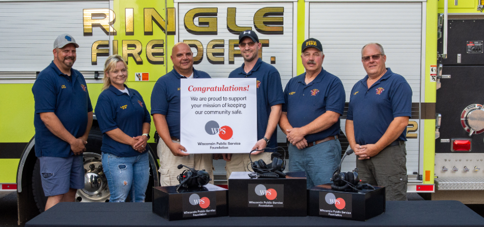 Members of the Ringle Fire Department in front of a table displaying new communications headsets.