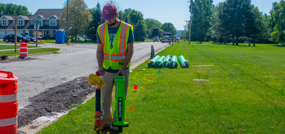 A WPS employee uses an electronic device to locate underground utility lines near a street.