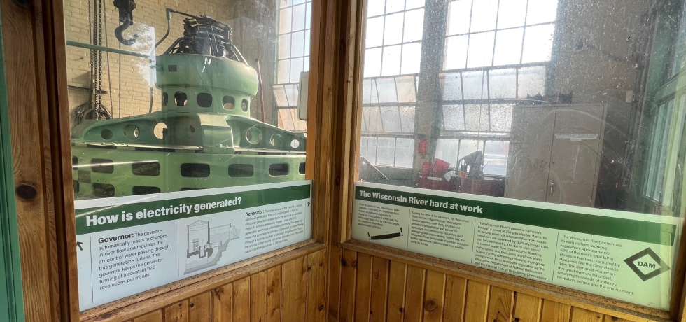 A view of a large, round and green generator behind glass at Otter Rapids Hydro.