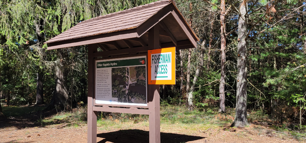 A wooden kiosk with an informational sign in a wooded area.