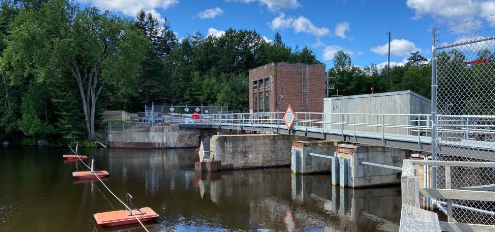 A view upstream of Otter Rapids Hydro next to a wooded area.