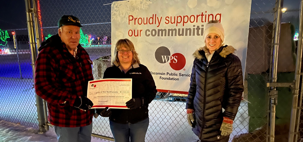 A man and woman hold a ceremonial check next to a WPS Foundation representative in front of a WPS sign at Lights of the Northwoods.