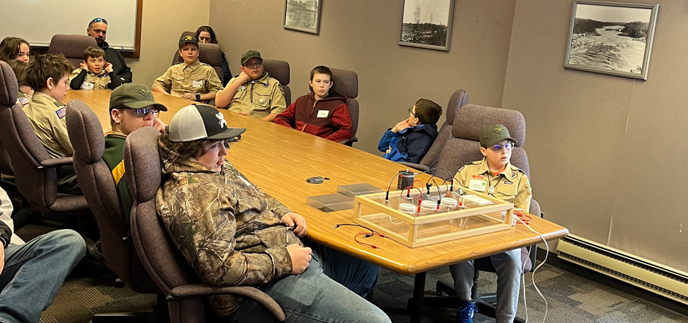 A group of Boy Scouts and parents listen to a discussion about electricity