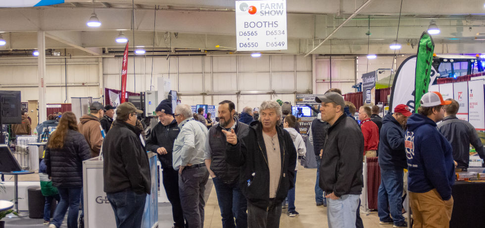 A crowd of people check out exhibitor booths inside a hangar at the WPS Farm Show.