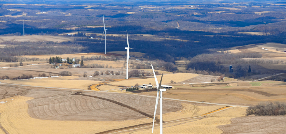 Three wind turbines aligned in a row along rural fields at the Red Barn Wind Park.