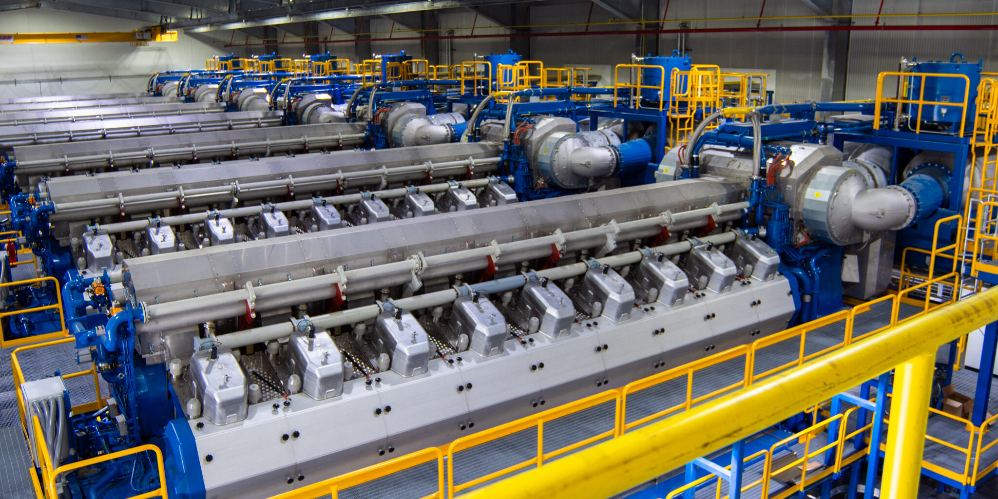 Blue and yellow industrial-size engines laid out in a row in a large building.