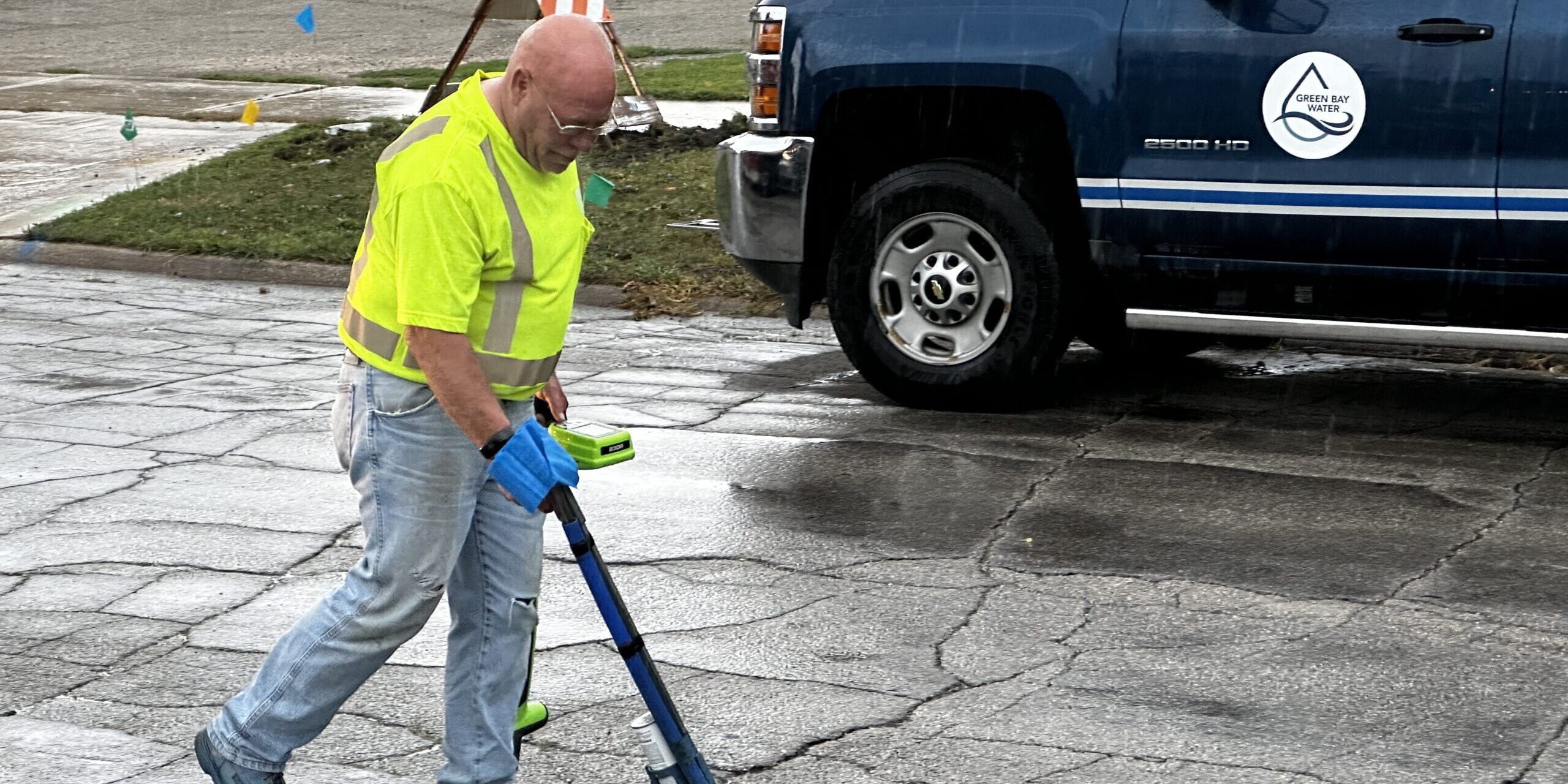 A man sprays blue paint onto a road to identify an underground water line.
