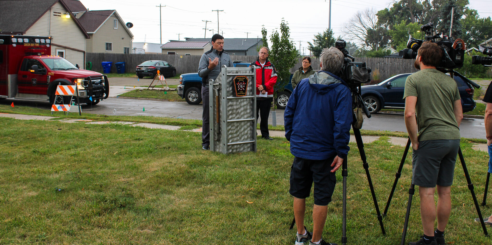 A group of TV video cameras film speech remarks on a grass lawn.