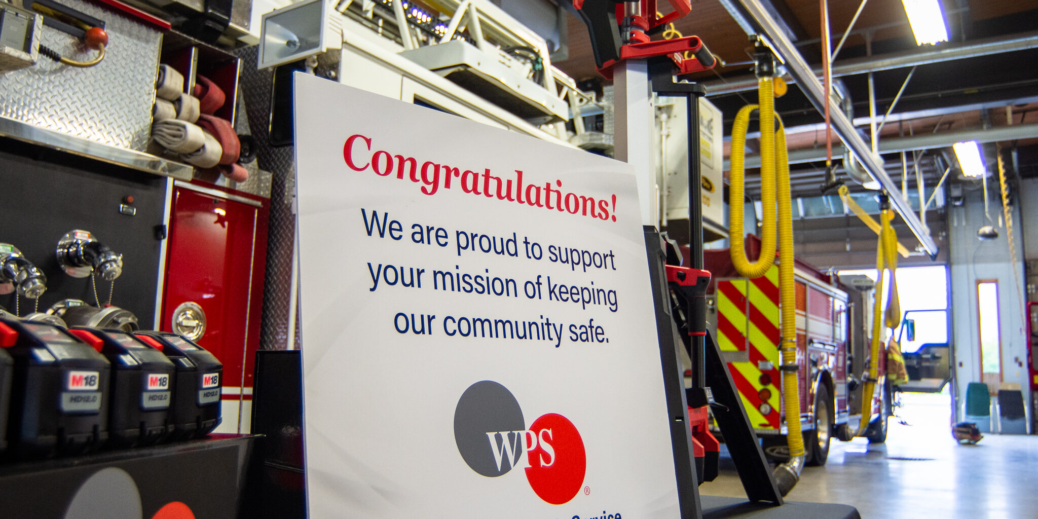 A congratulatory sign displayed next to a red emergency scene light tower inside a fire department garage.