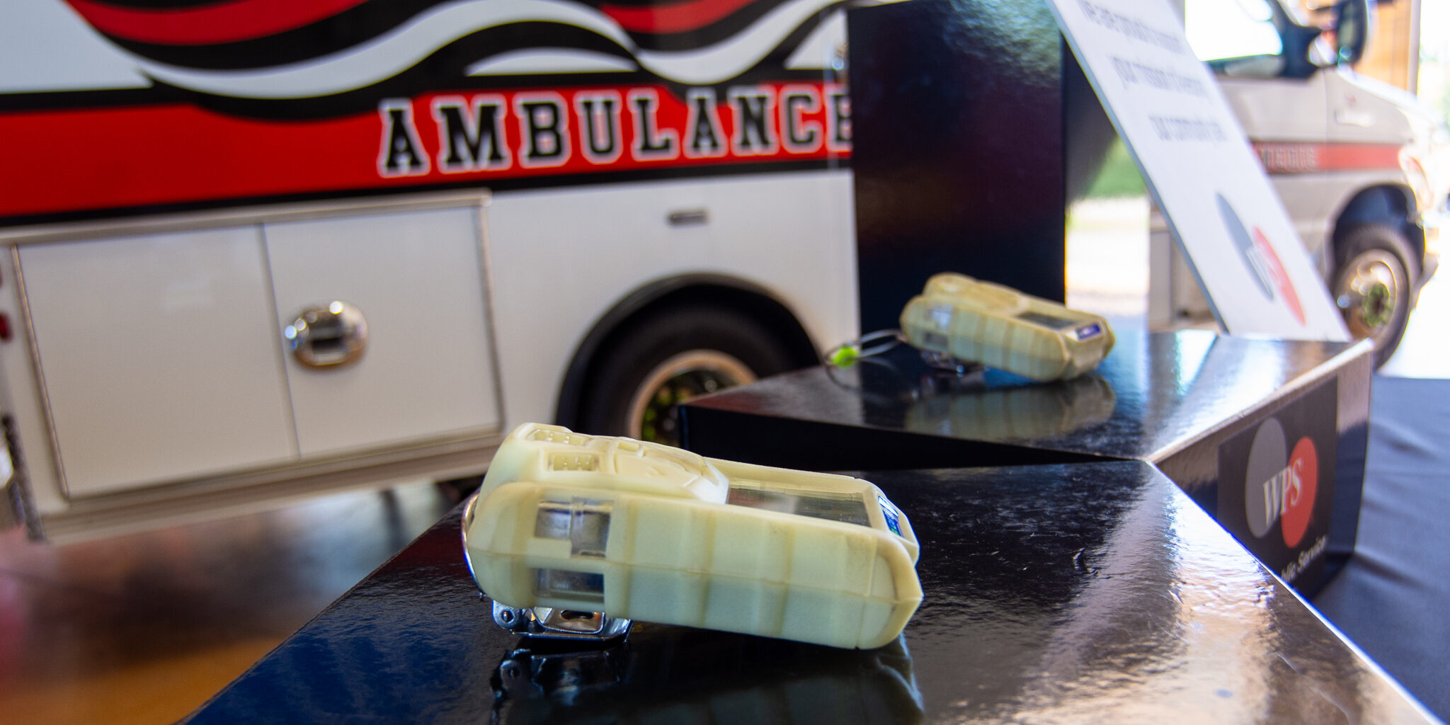 Small grey multi-gas detectors sit on top of black boxes next to an ambulance.