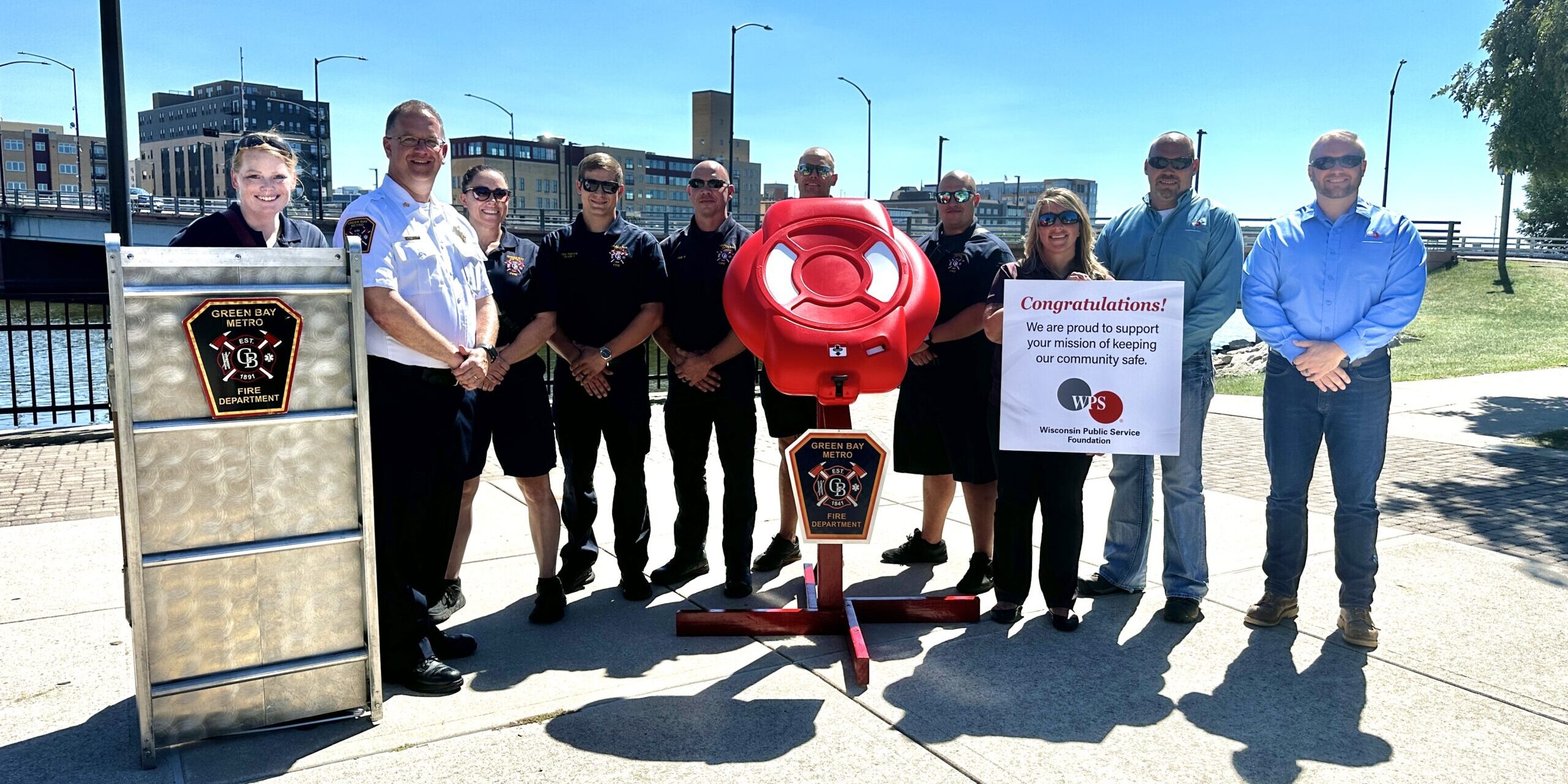 A group of men and women firefighters and WPS Foundation representatives stand next to a red life preserver ring on a stand.