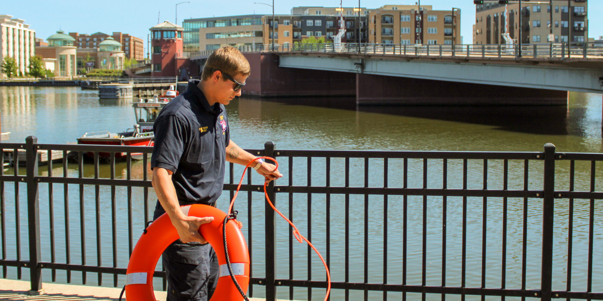A male firefighter holds an orange life preserver ring on a pier.