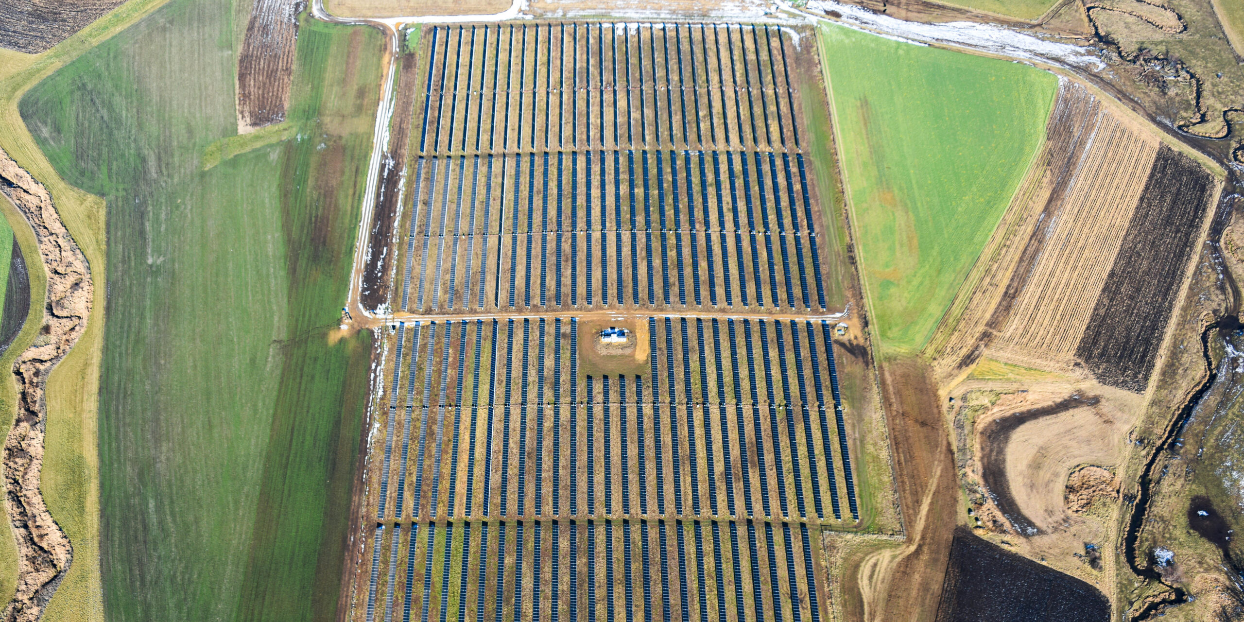 Aerial view of a rectangular grouping of solar panels near fields.
