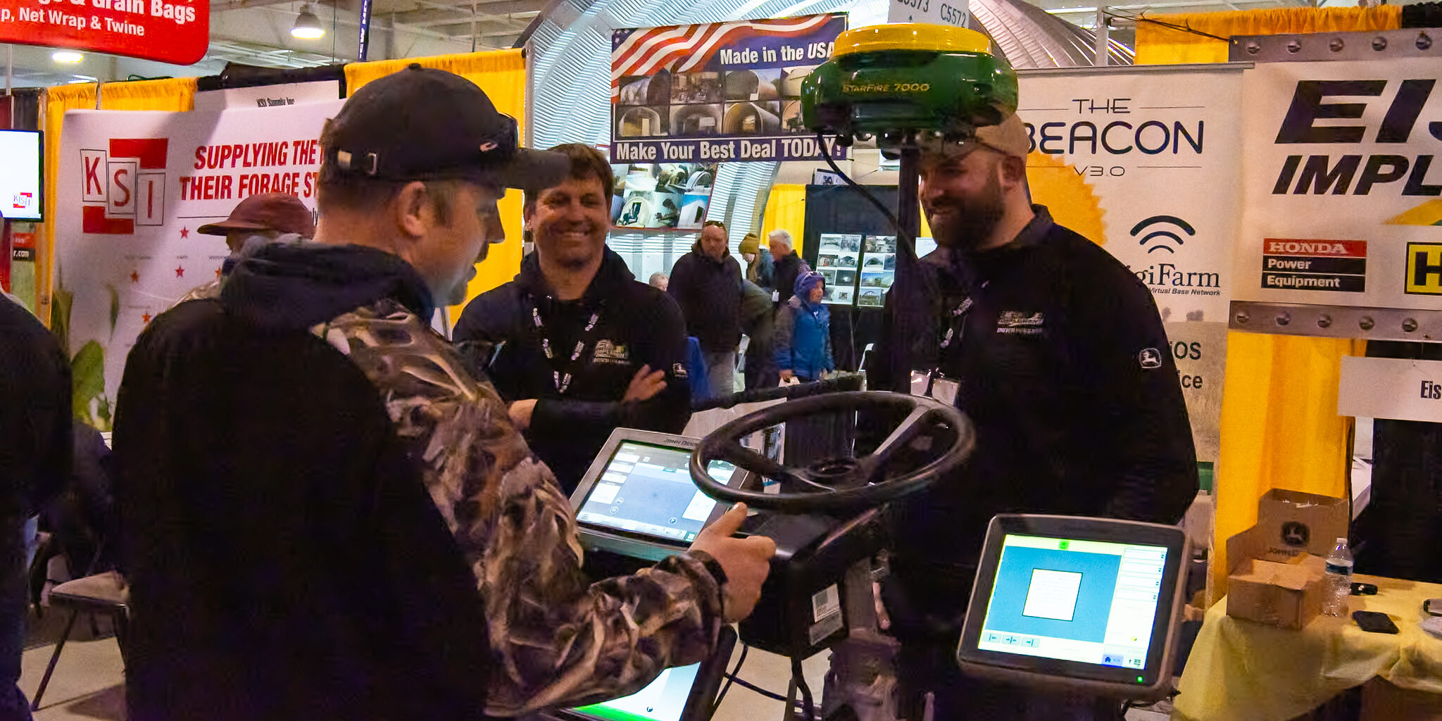 A man looks at a digital steering display while speaking to two representatives of an exhibitor at the WPS Farm Show.