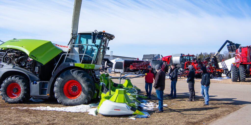 A group of people look at a large green forage harvester at the WPS Farm Show.