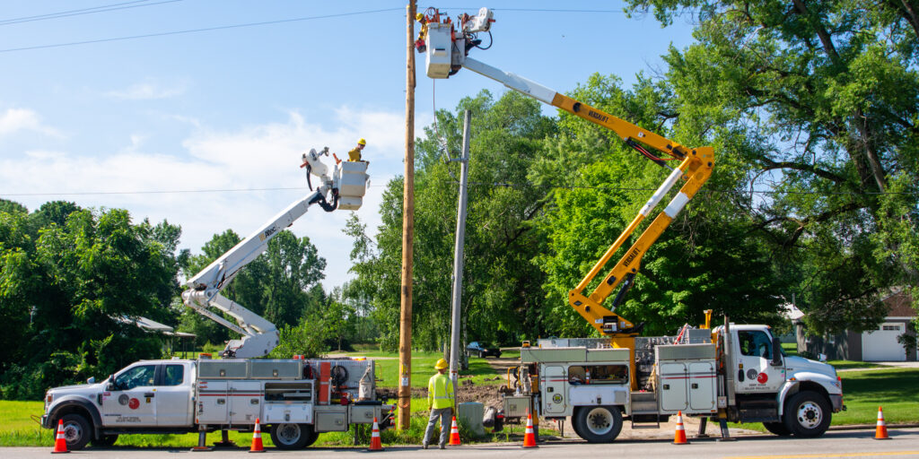 Two bucket trucks with lineworkers in the buckets parked next to a utility pole.