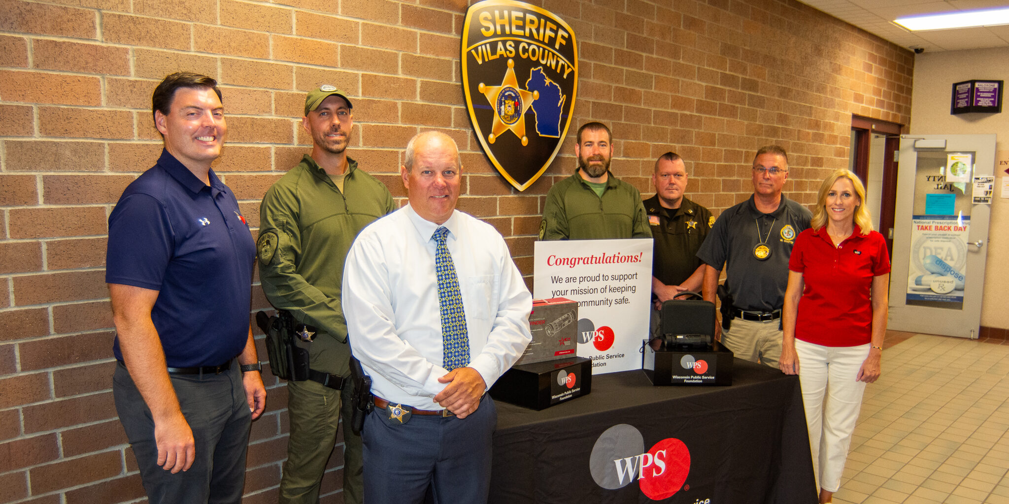 WPS representatives join a small group of Vilas County Sheriff's Office members for a photo next to a thermal imaging device lying on a table.