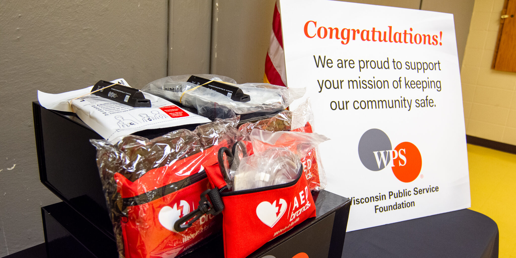 AED and first aid equipment arranged on top of black boxes with the WPS Foundation logo on them. Next to the boxes is a congratulatory sign.