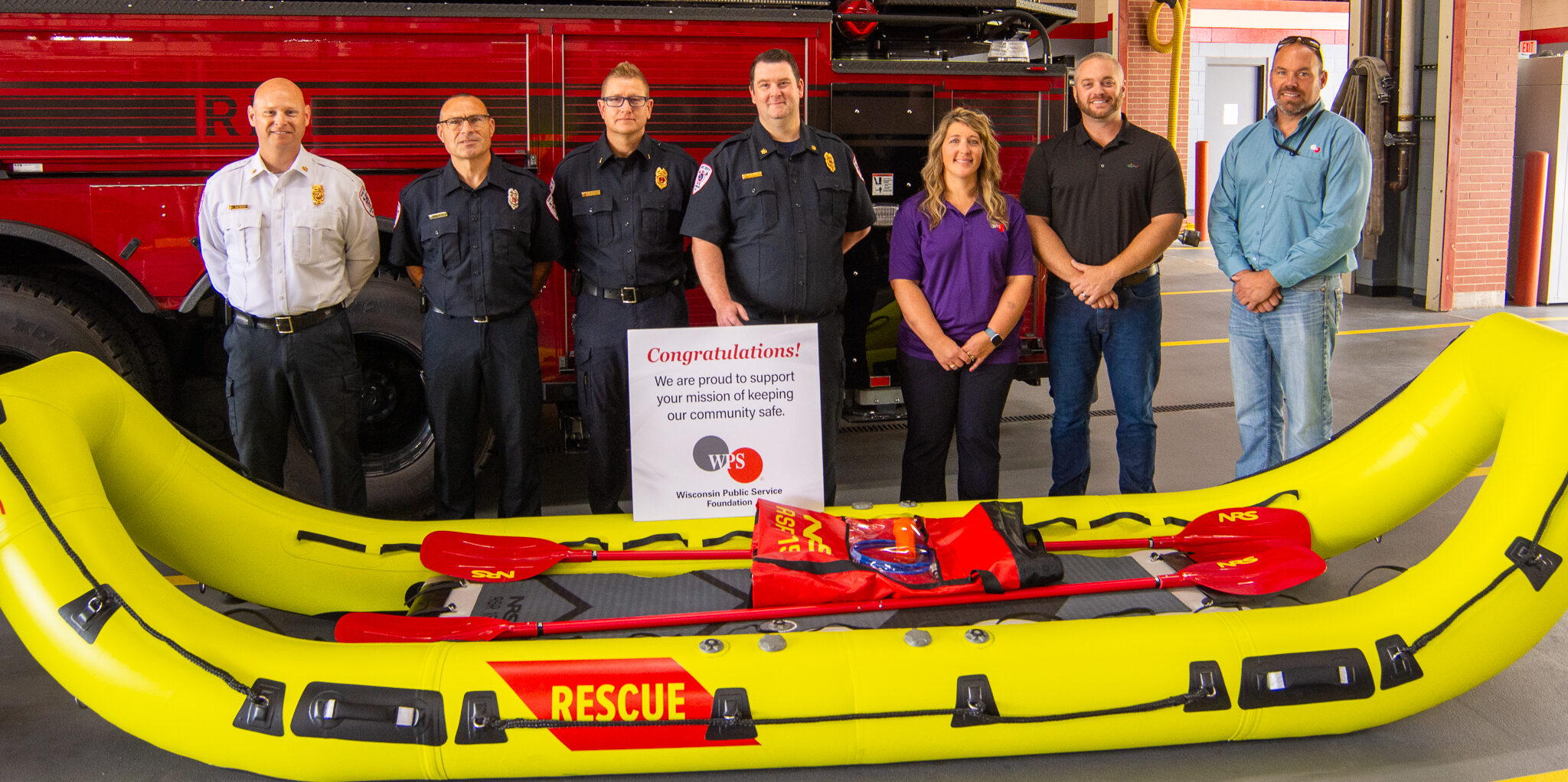 WPS employees and Howard Fire Rescue Department firefighters stand behind a yellow and red rapid deployment watercraft.