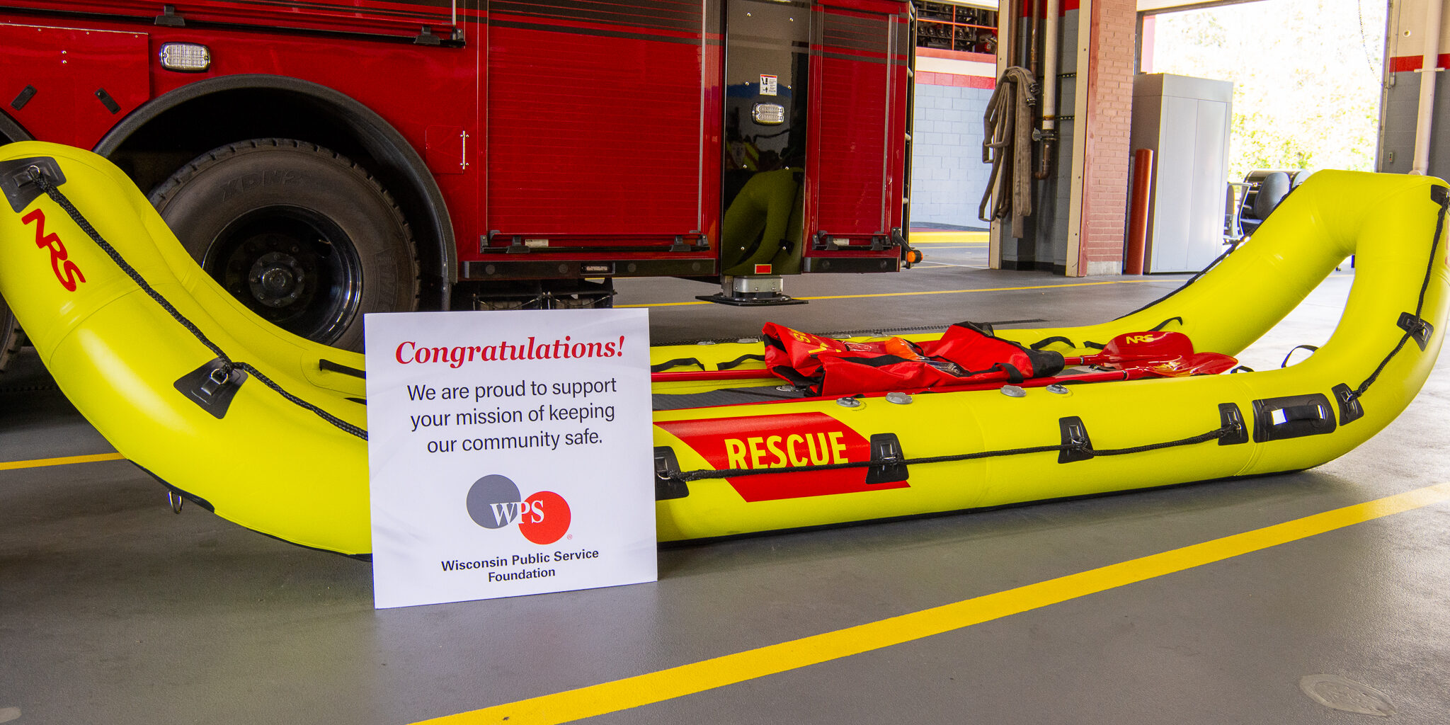 A large yellow and red inflatable rescue boat lying in front of a fire engine.