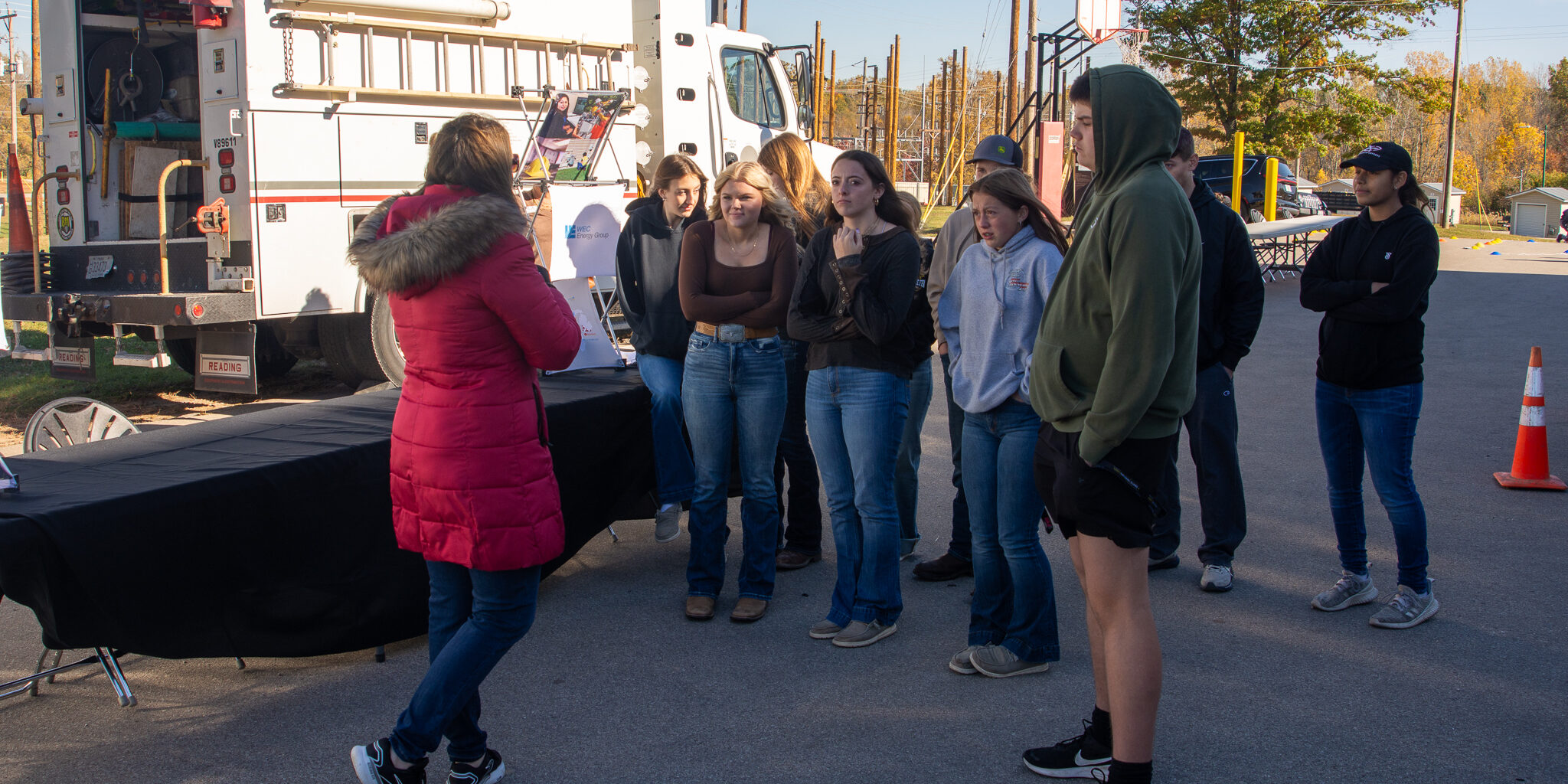 A woman in a red coat speaks with a small group of high school students near a large WPS vehicle.