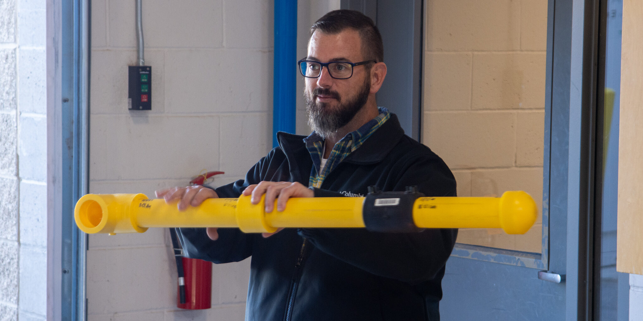 A male WPS employee discusses joining two yellow plastic pipes together inside a large room.