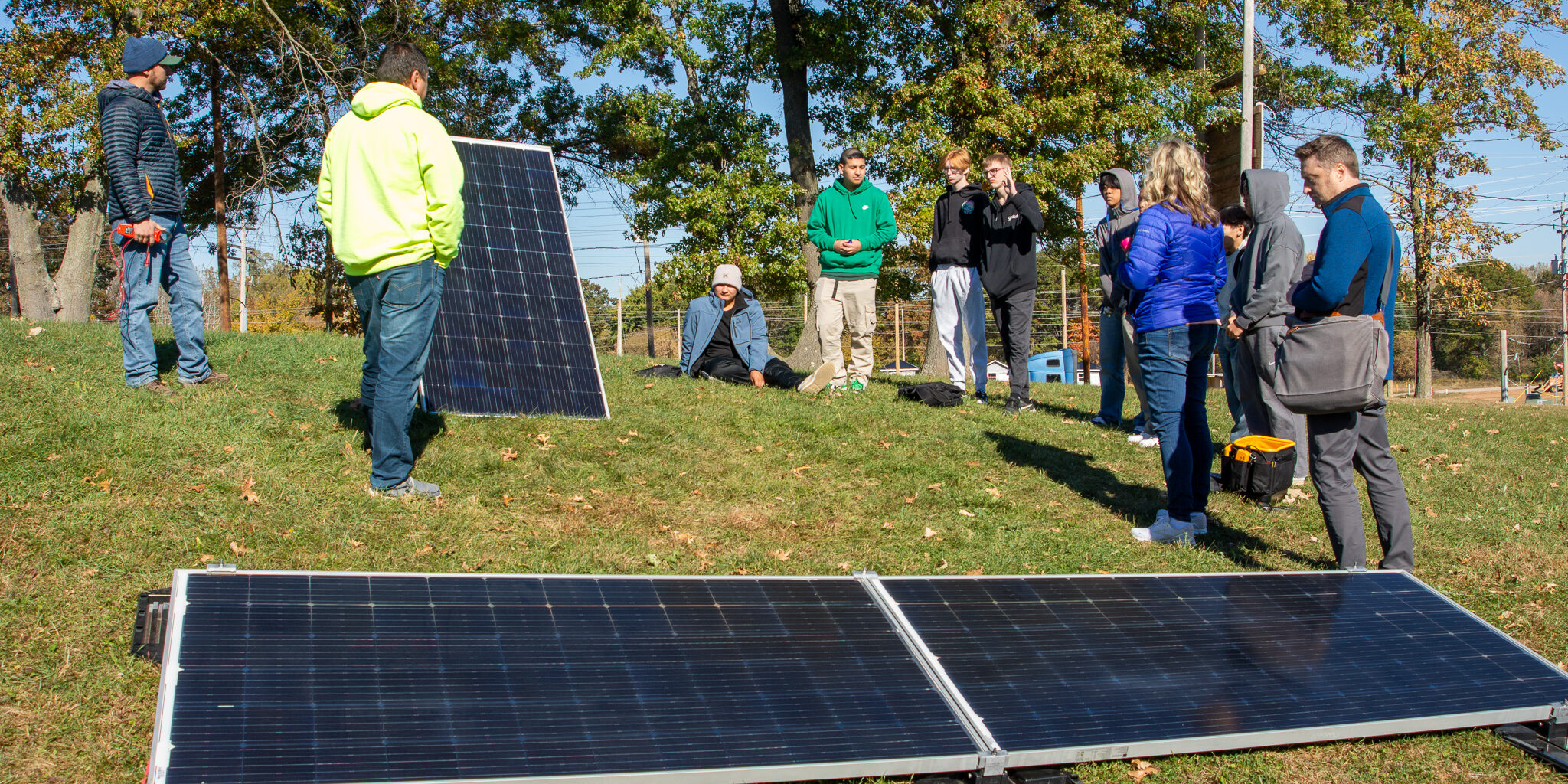 A group of students listens to electricians on a sunny day describe how solar panels operate.