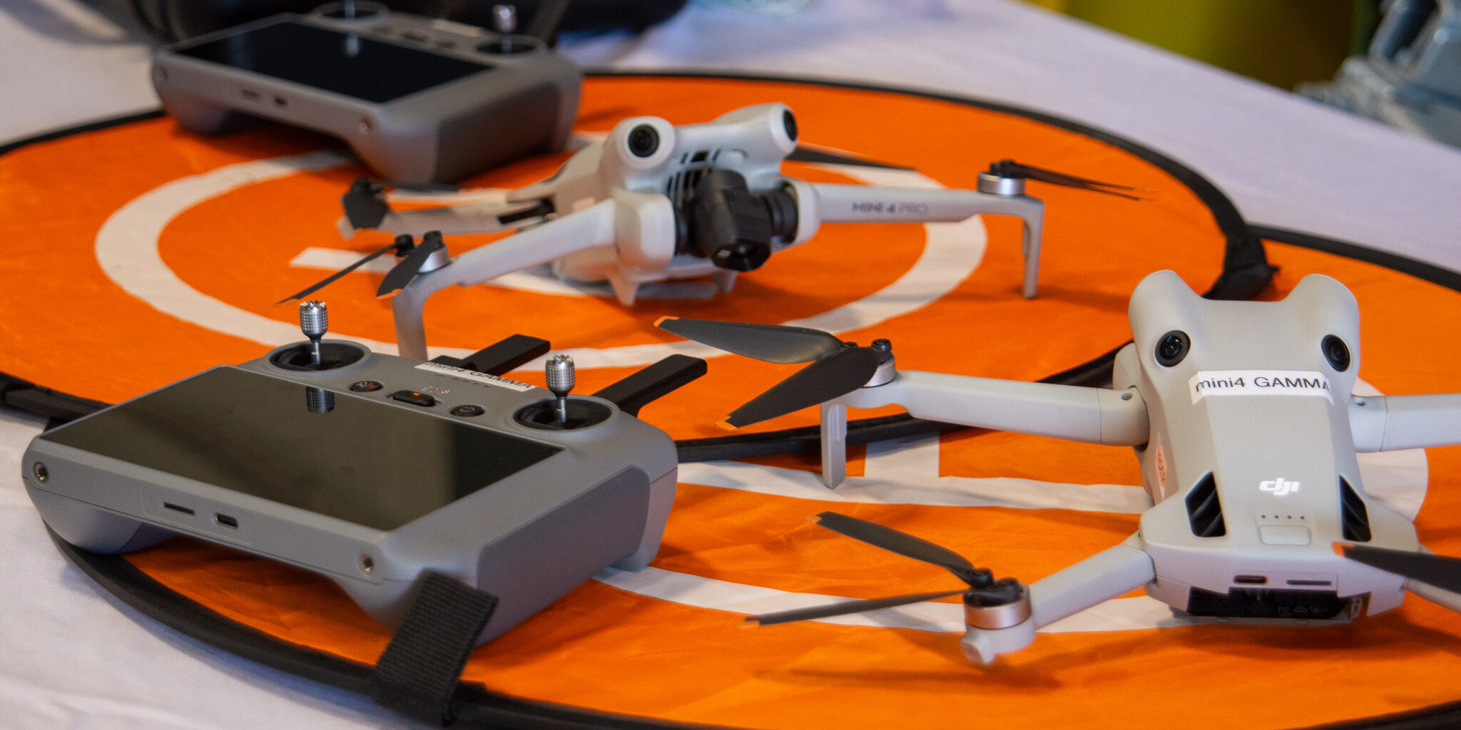 Drones and remote controls lie on orange circular mats on a table.