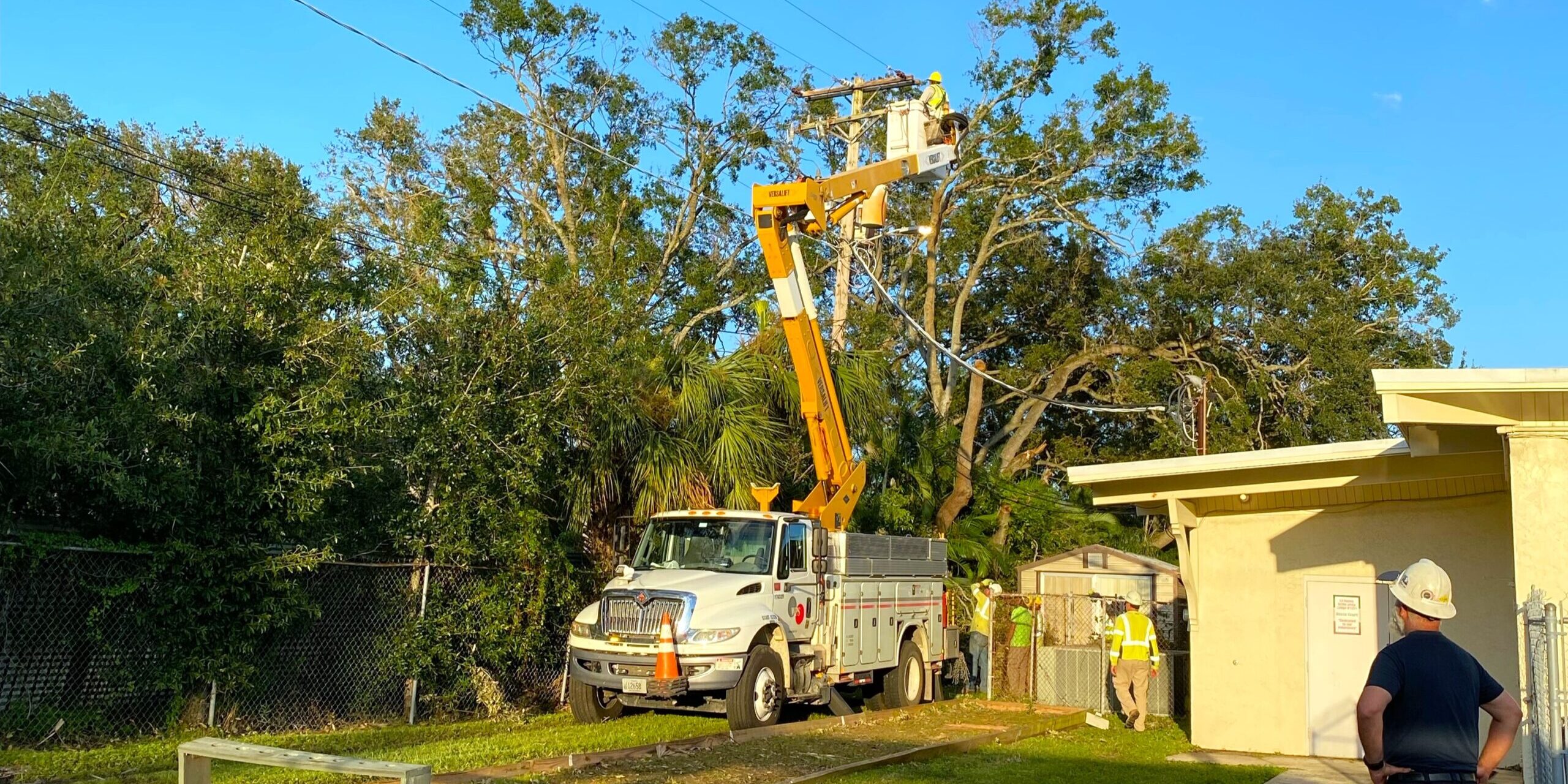 A group of WPS lineworkers repairs a power line in a backyard as another lineworker looks on.