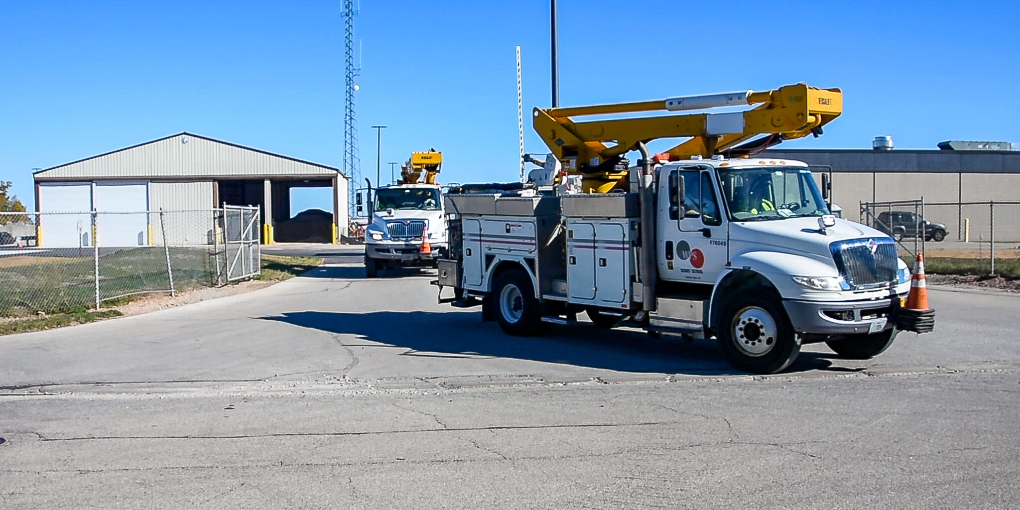 Utility bucket trucks drive away from large warehouse buildings