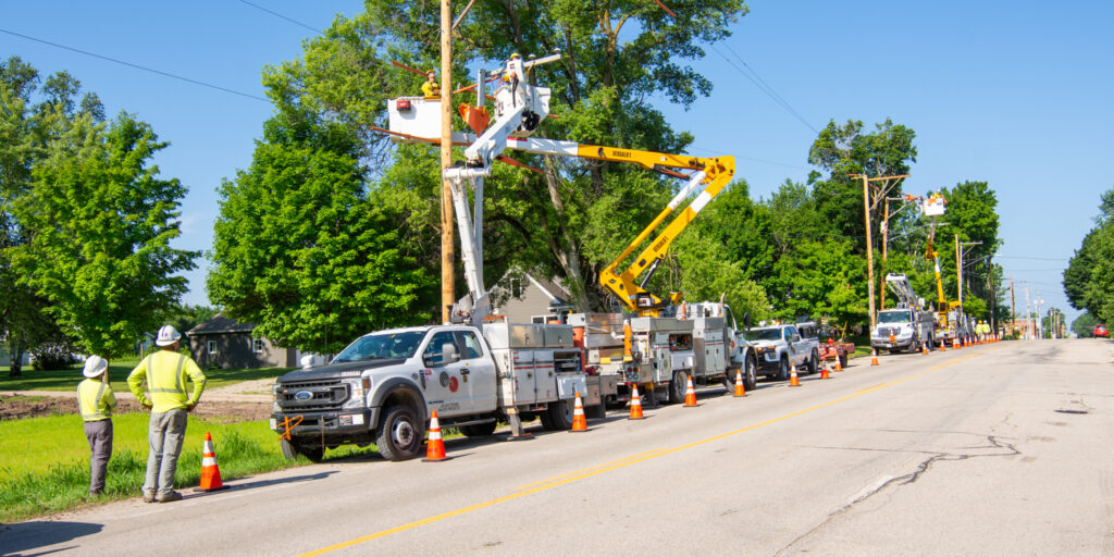 A row of WPS trucks and multiple lineworkers work on overhead power lines.