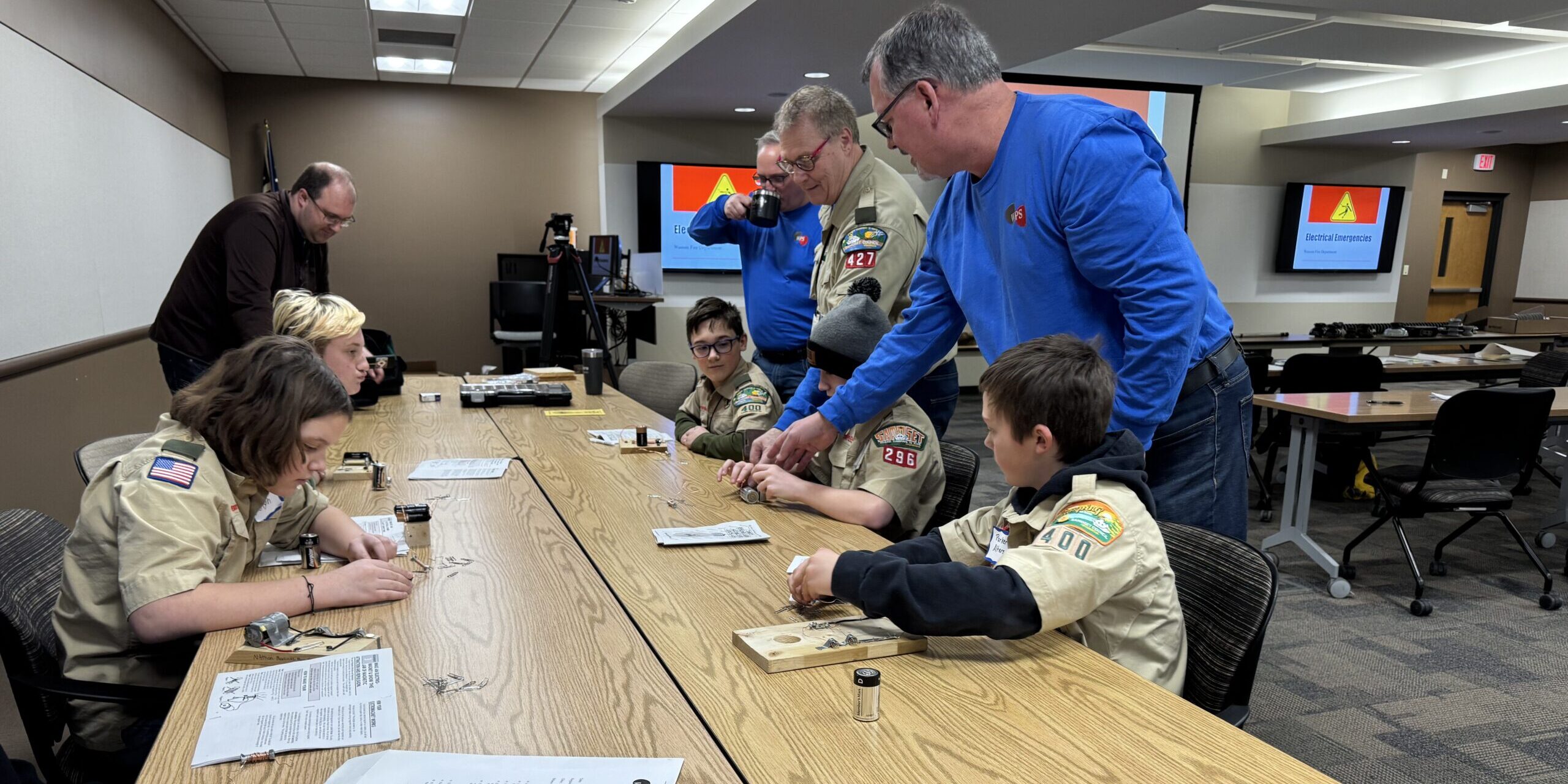 WPS employees assist Scouts with electric circuit projects along a long table.