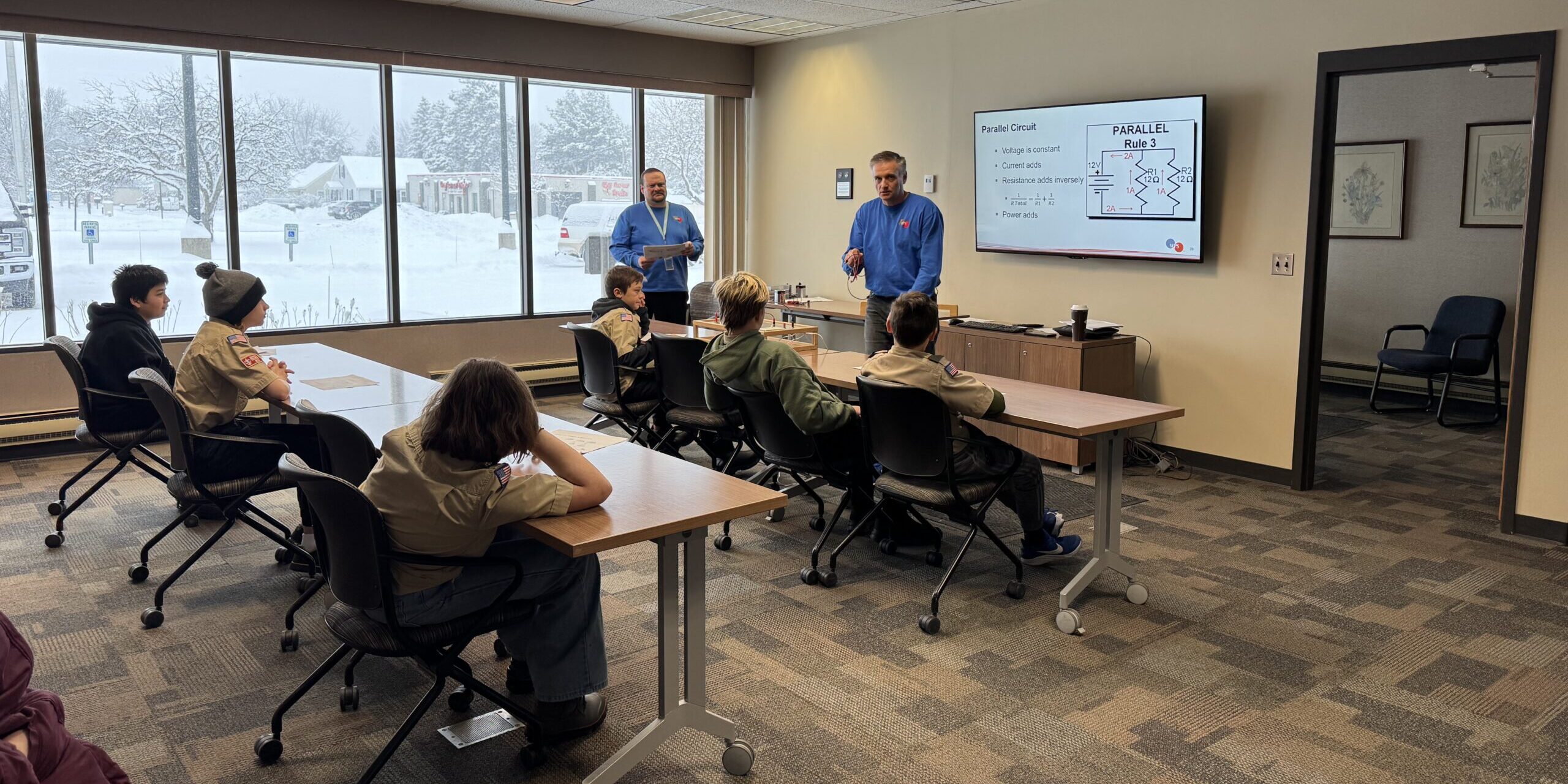 WPS employees speak about electric circuits with Scouts sitting at long horizontal tables.