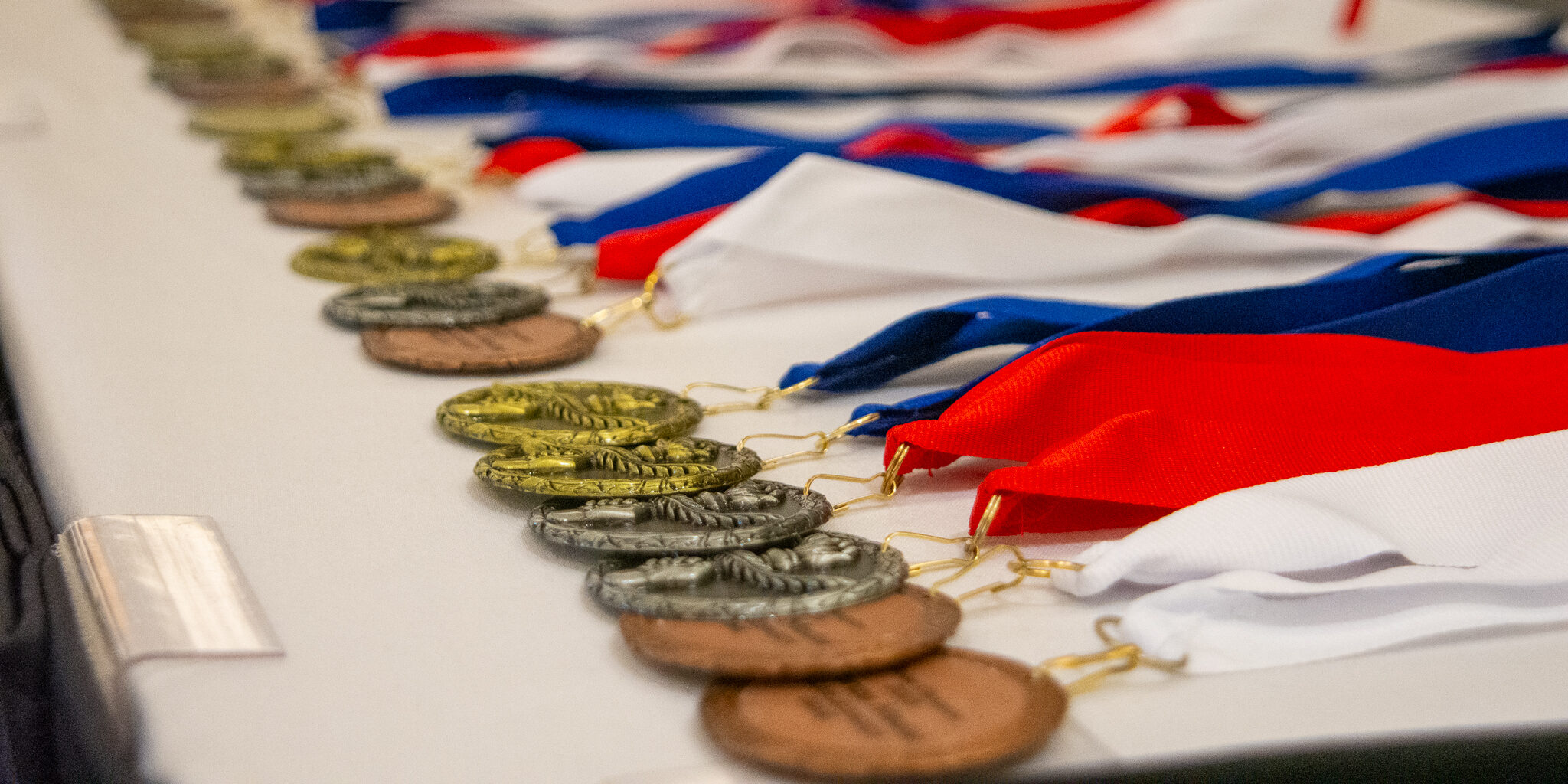 Gold, silver and bronze medals lying in a row on a table.
