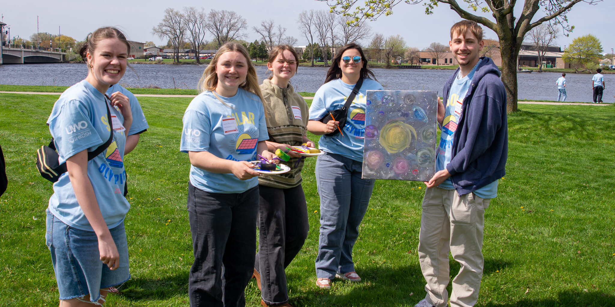 High school students display a solar-themed painting on a sunny day.