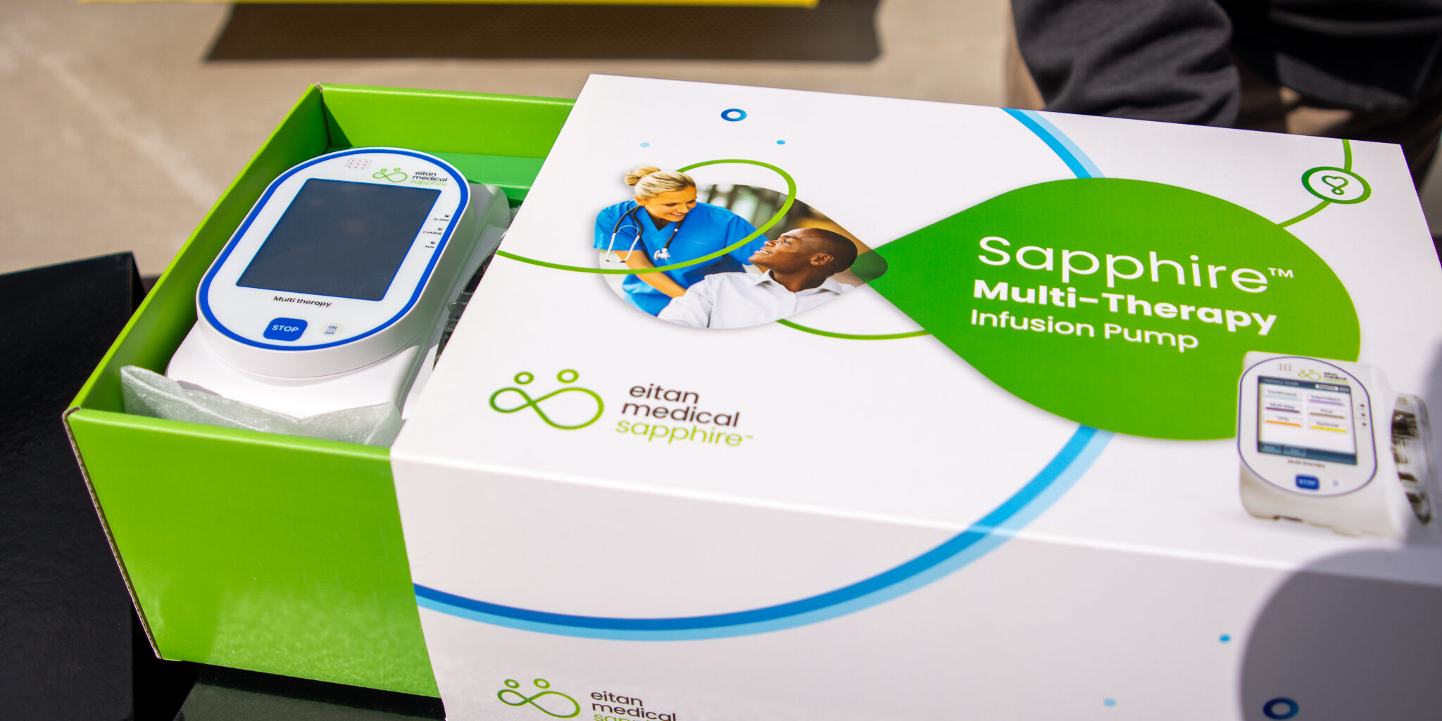 A close-up photo of a small medical infusion pump resting inside a green and white box.