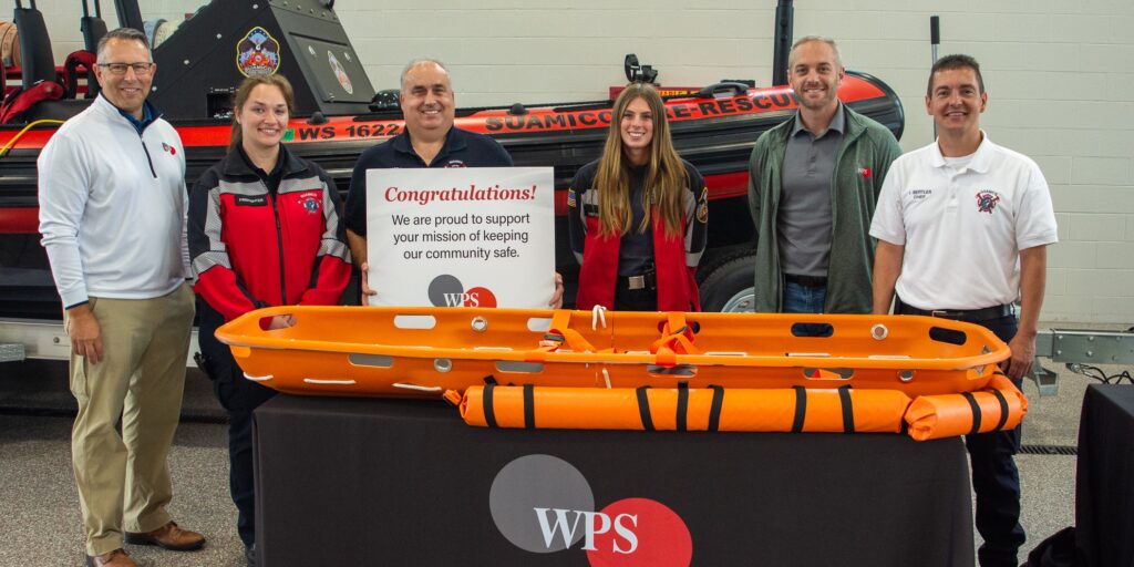A small group of men and women stand behind an orange rescue stretcher on top of a table.