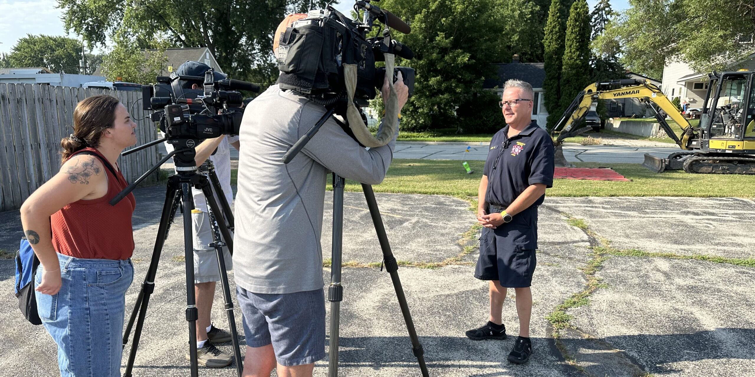 A Green Bay Metro Fire Department firefighter speaks with TV news crews in a parking lot near a digging site.