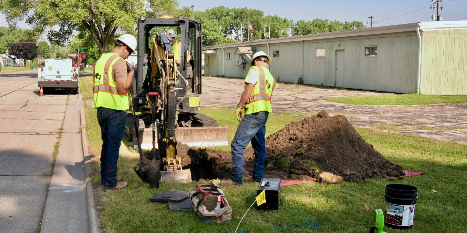 WPS natural gas mechanics dig a hole with a backhoe and shovels near a residential street.