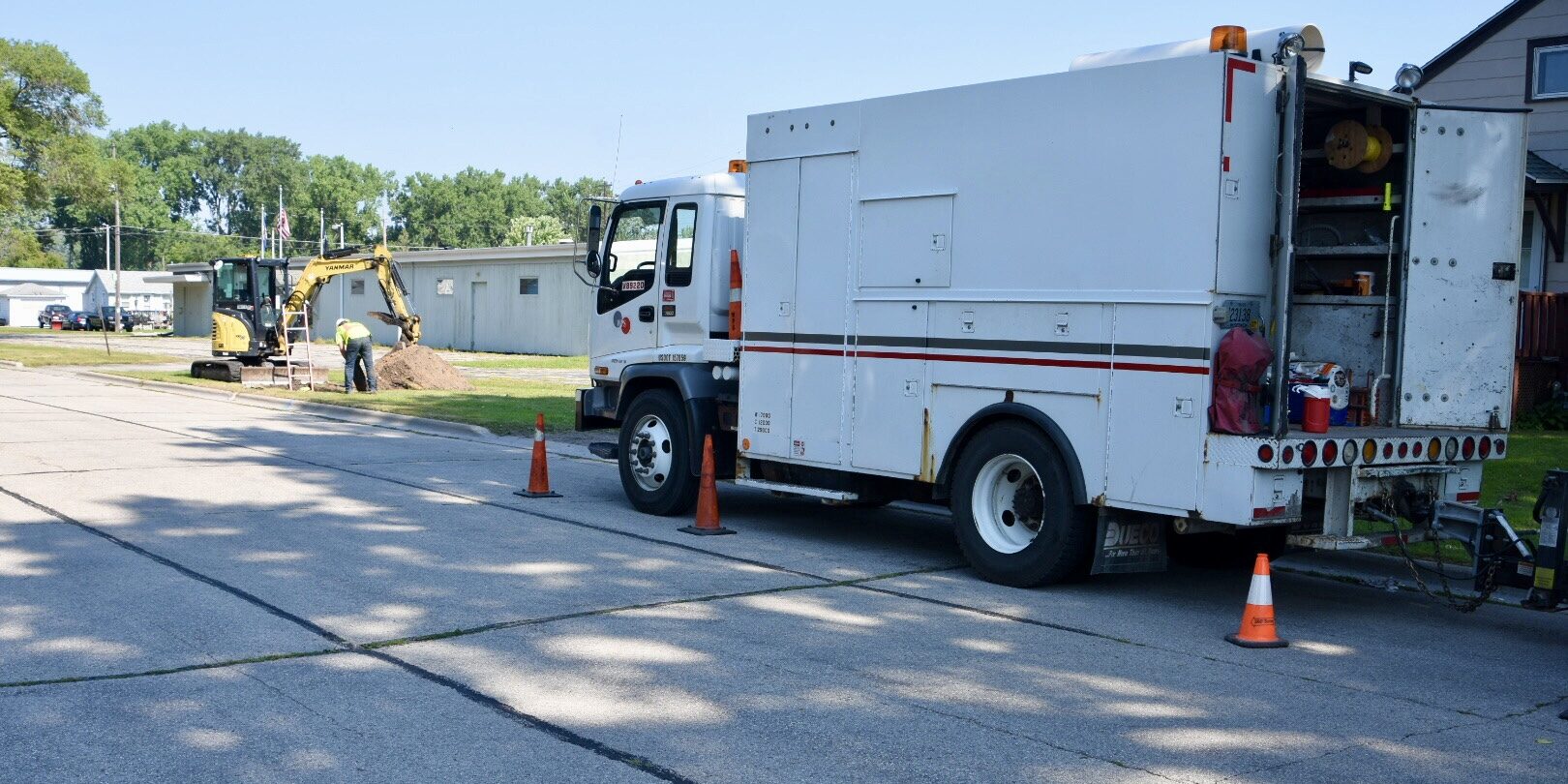 A large WPS box truck parked along a street near a backhoe digging in a grassy area.