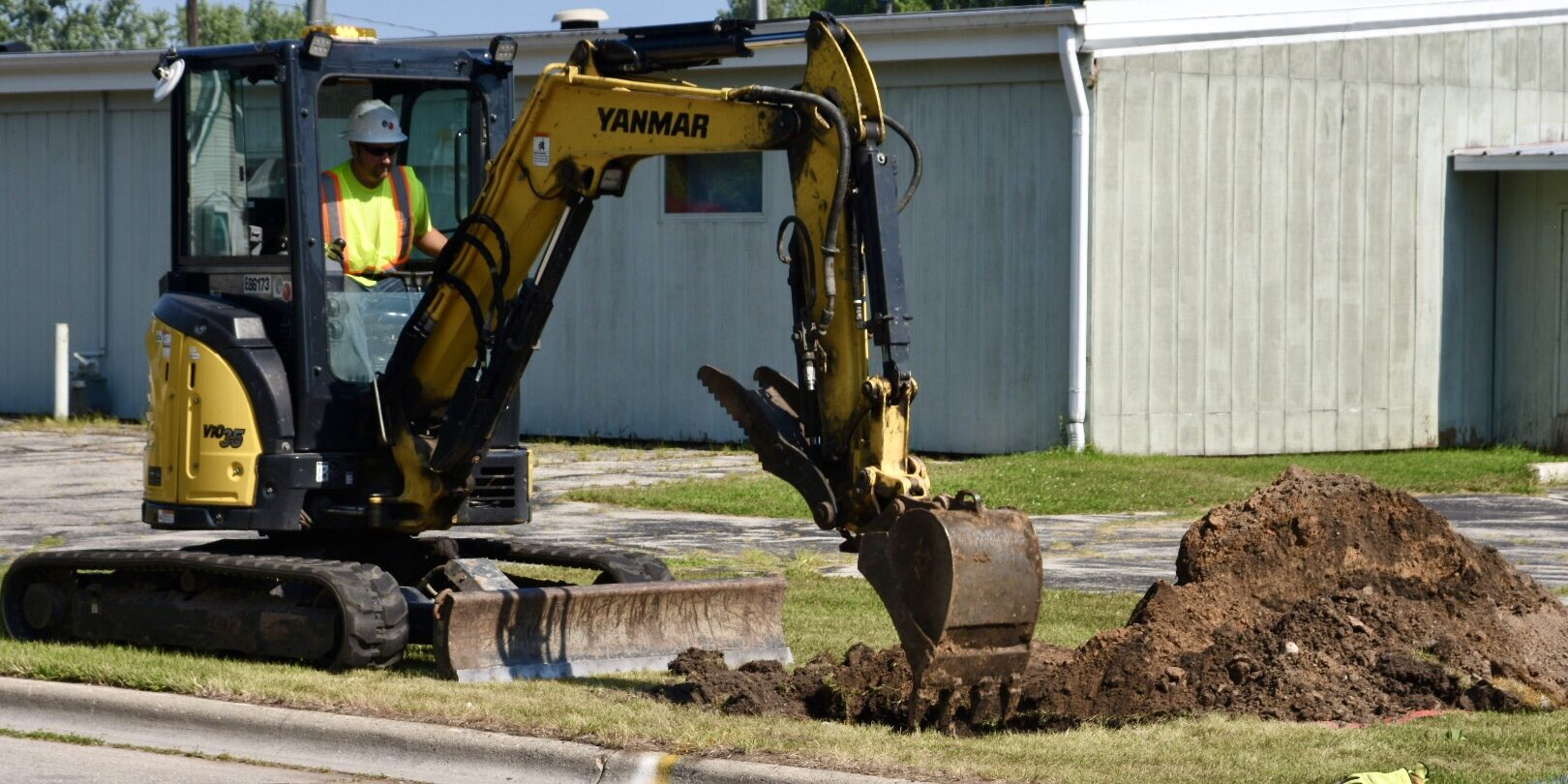 A WPS worker using a backhoe to dig a hole in a grassy area near a street.