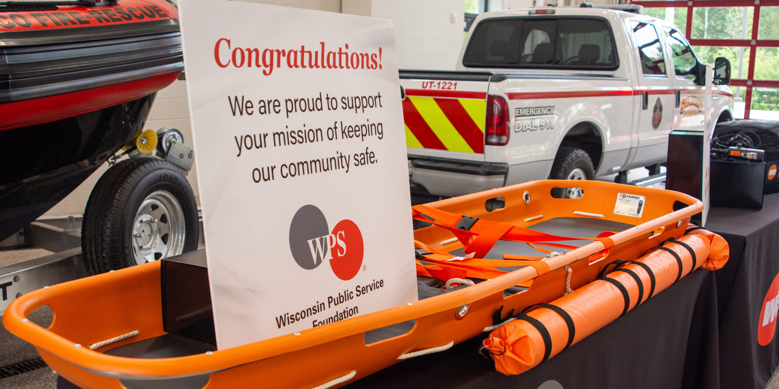 A congratulatory sign with the WPS Foundation logo on it sits inside an orange water rescue basket resting on a table.