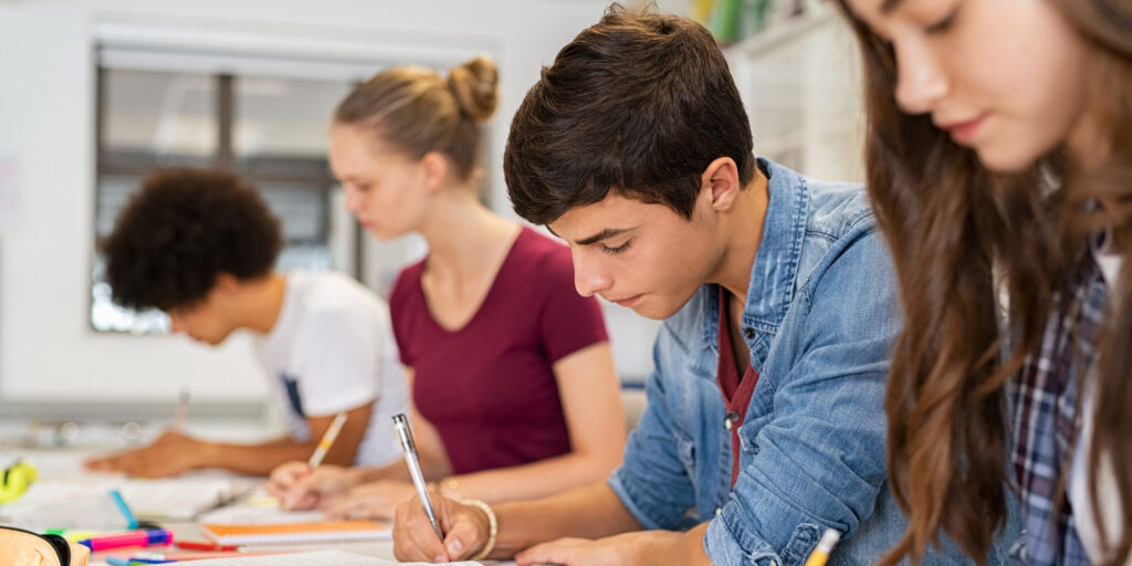 A group of male and female college students write and study inside a classroom.