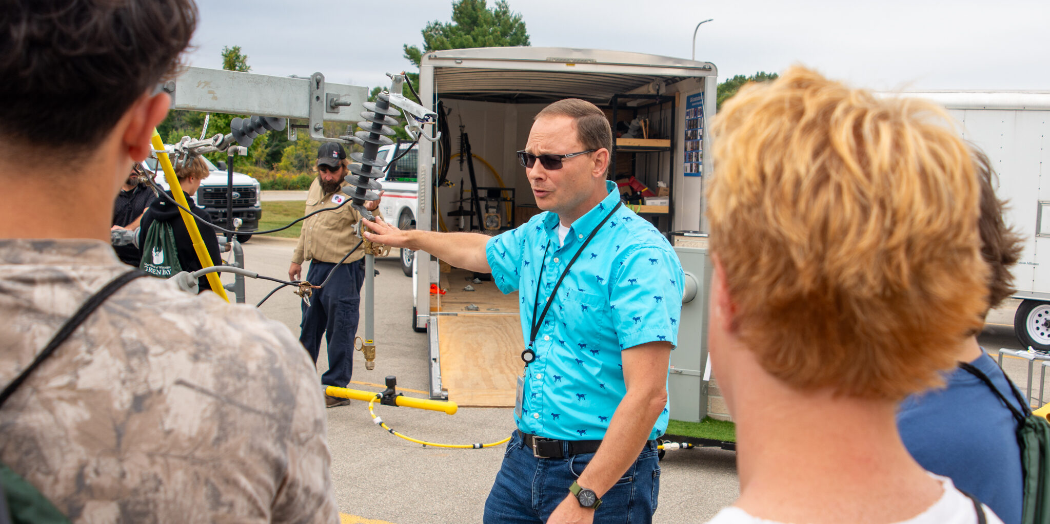 A WPS employee wearing a blue shirt talks about electricity to a group of high school students.