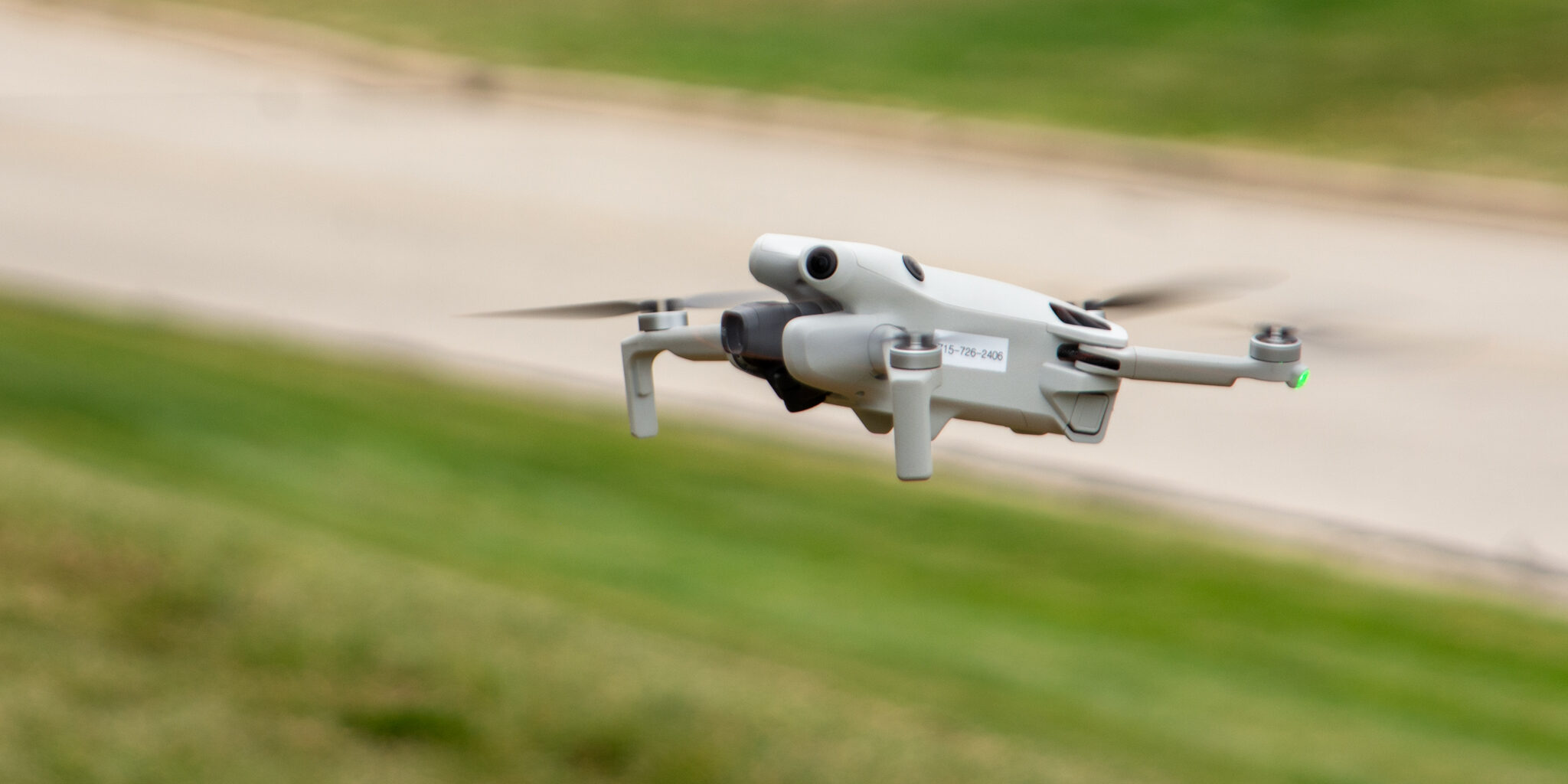 A small grey aerial drone hovers a few feet off the ground.