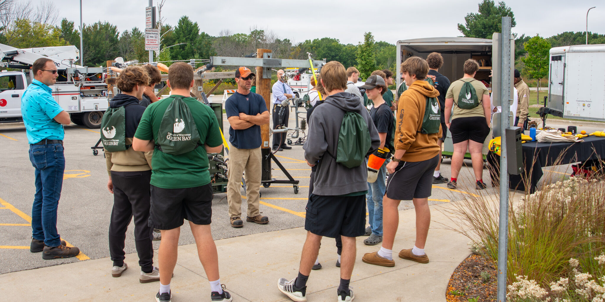 A group of high school students listens to a WPS employee speak around a life-sized electric system display.